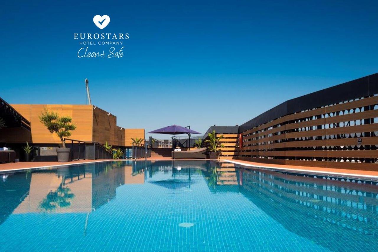 Eurostars Palace Cordoba Luaran gambar The photo shows an outdoor swimming pool with clear, blue water, reflecting the blue sky above. The pool area is surrounded by modern architectural features, including wooden slats and potted plants. There is also a purple umbrella providing shade. T