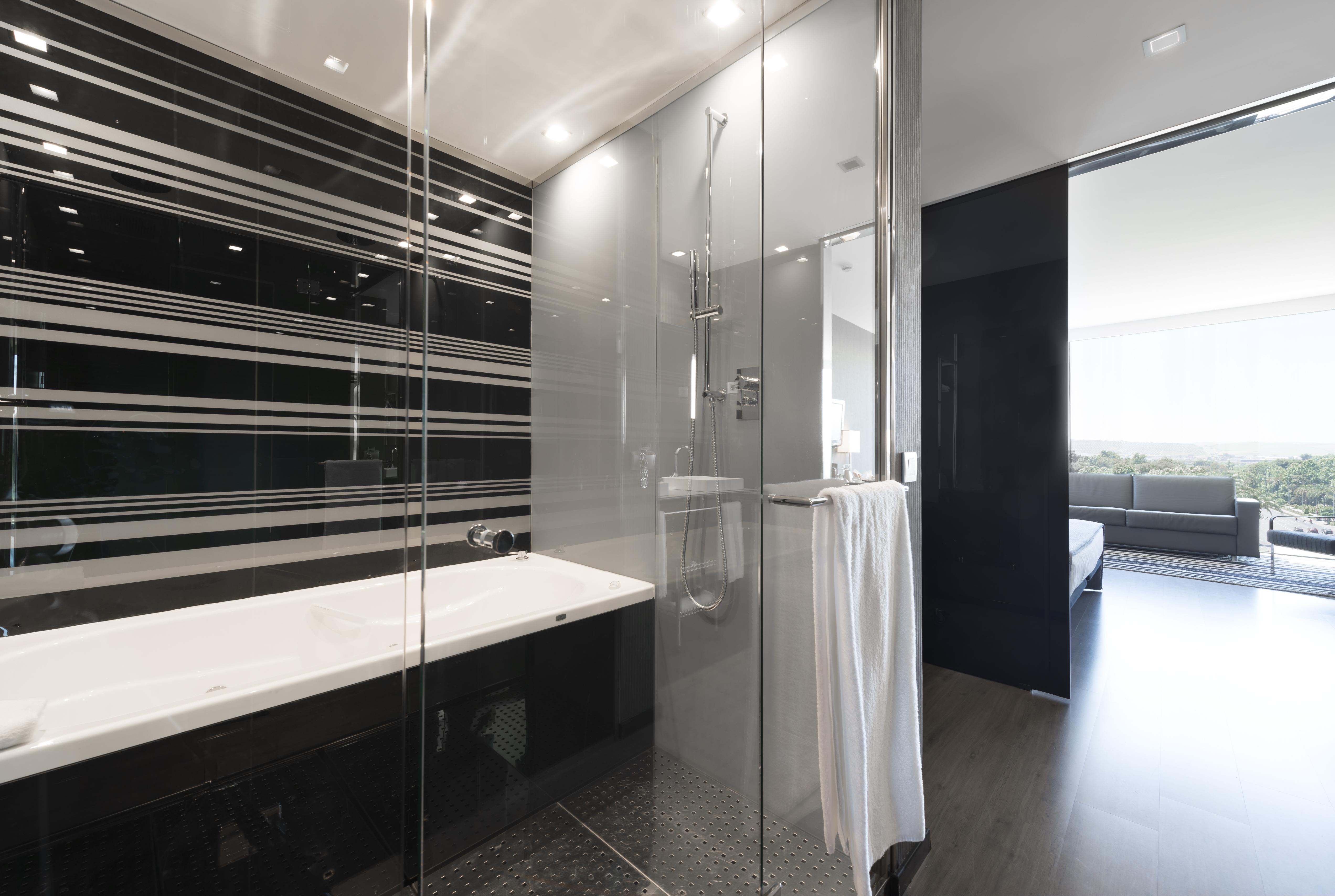 Eurostars Palace Cordoba Luaran gambar The photo shows a modern bathroom featuring a sleek design. On one side, there is a glass-enclosed shower with contemporary fixtures. Adjacent to it, there's a stylish bathtub with a clean, white surface. The walls are decorated with a striking patte