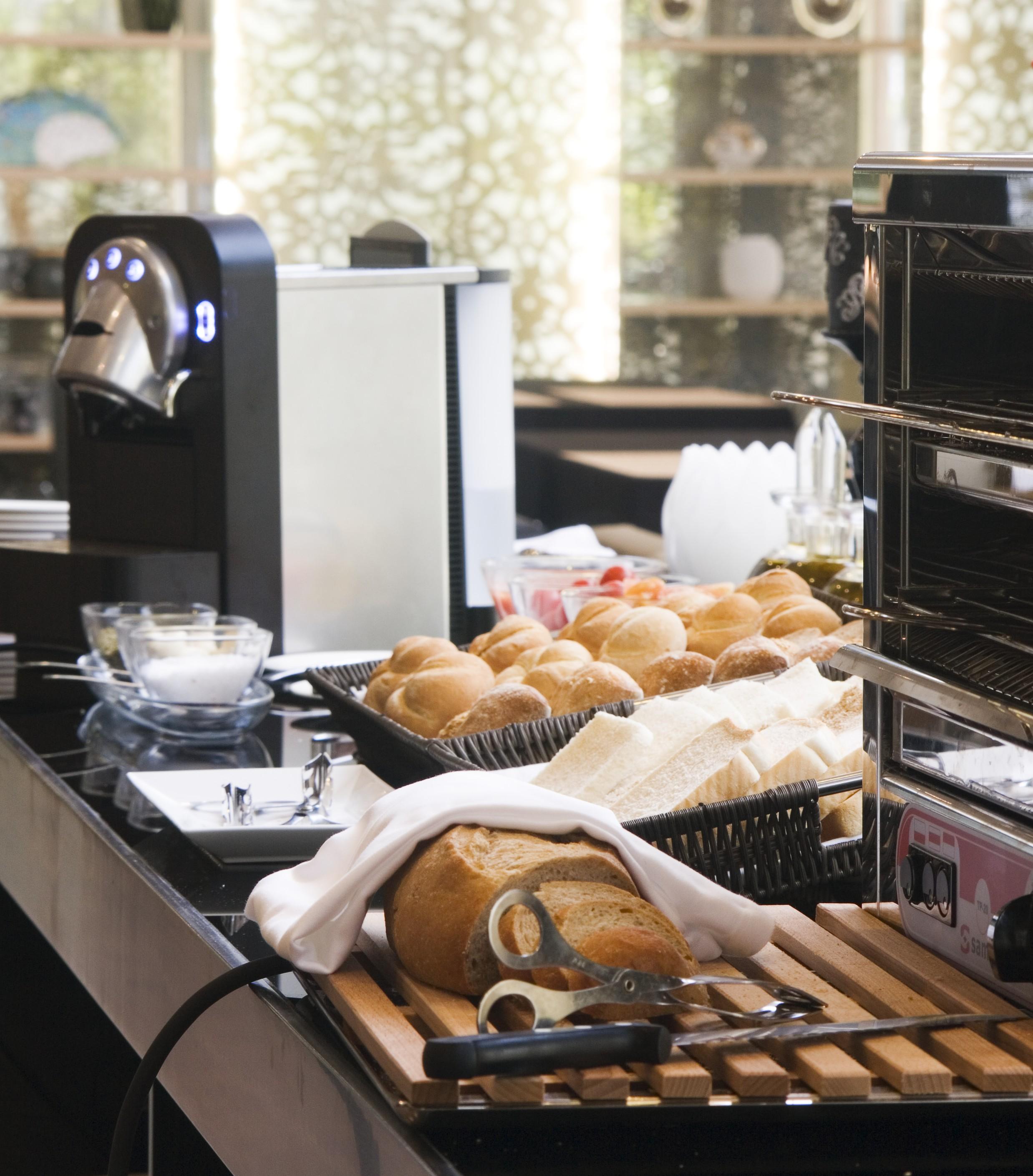 Eurostars Palace Cordoba Luaran gambar The photo shows a dining setup featuring various food items. On the left, there is a coffee machine, and in the foreground, there is a basket of freshly baked bread rolls. Next to the rolls, there are slices of bread arranged neatly. In the backgroun