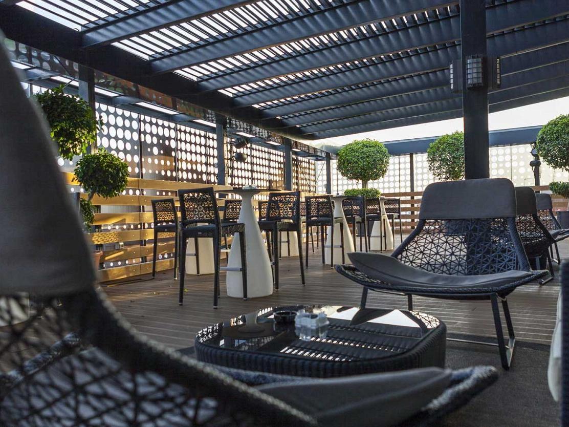 Eurostars Palace Cordoba Luaran gambar The photo shows a modern outdoor seating area, likely on a rooftop or terrace. It features stylish black wicker chairs and tables arranged for comfort. The area is partially shaded by a striped overhead structure, creating a relaxing atmosphere. Pott