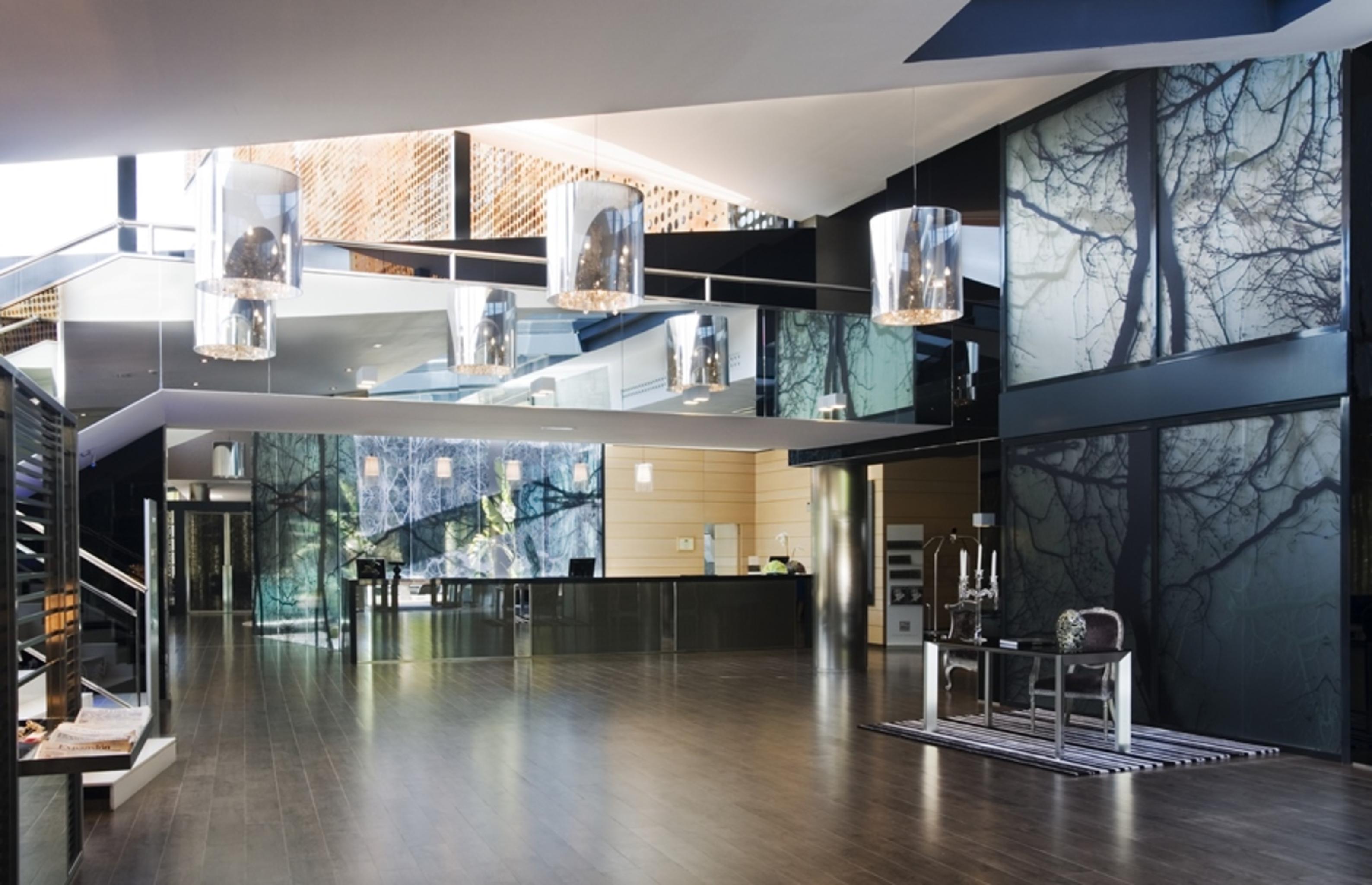 Eurostars Palace Cordoba Dalaman gambar The photo shows a modern interior space, likely an entrance or lobby area. The design features:

- A spacious layout with a polished wooden floor.
- Large glass panels that reflect light, creating an open and airy feel.
- Artistic wall décor that inc