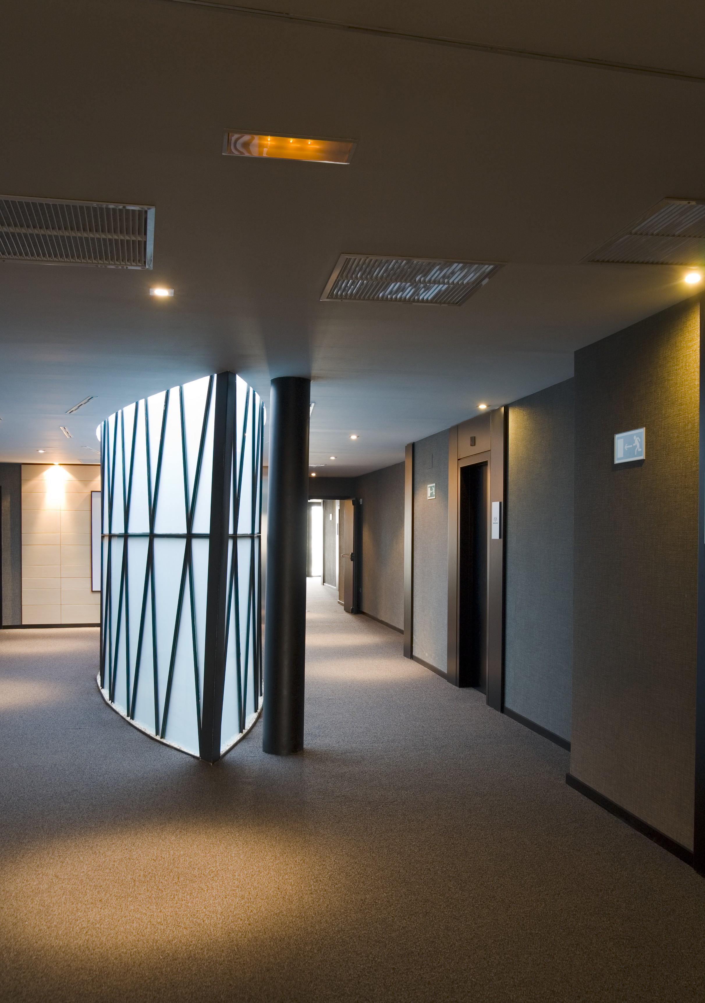 Eurostars Palace Cordoba Luaran gambar The photo shows a modern indoor corridor featuring a smooth, curved wall with a geometric pattern. The corridor is well-lit with recessed ceiling lights, and the floor is carpeted. There are doors leading to elevators on the right side, and the walls