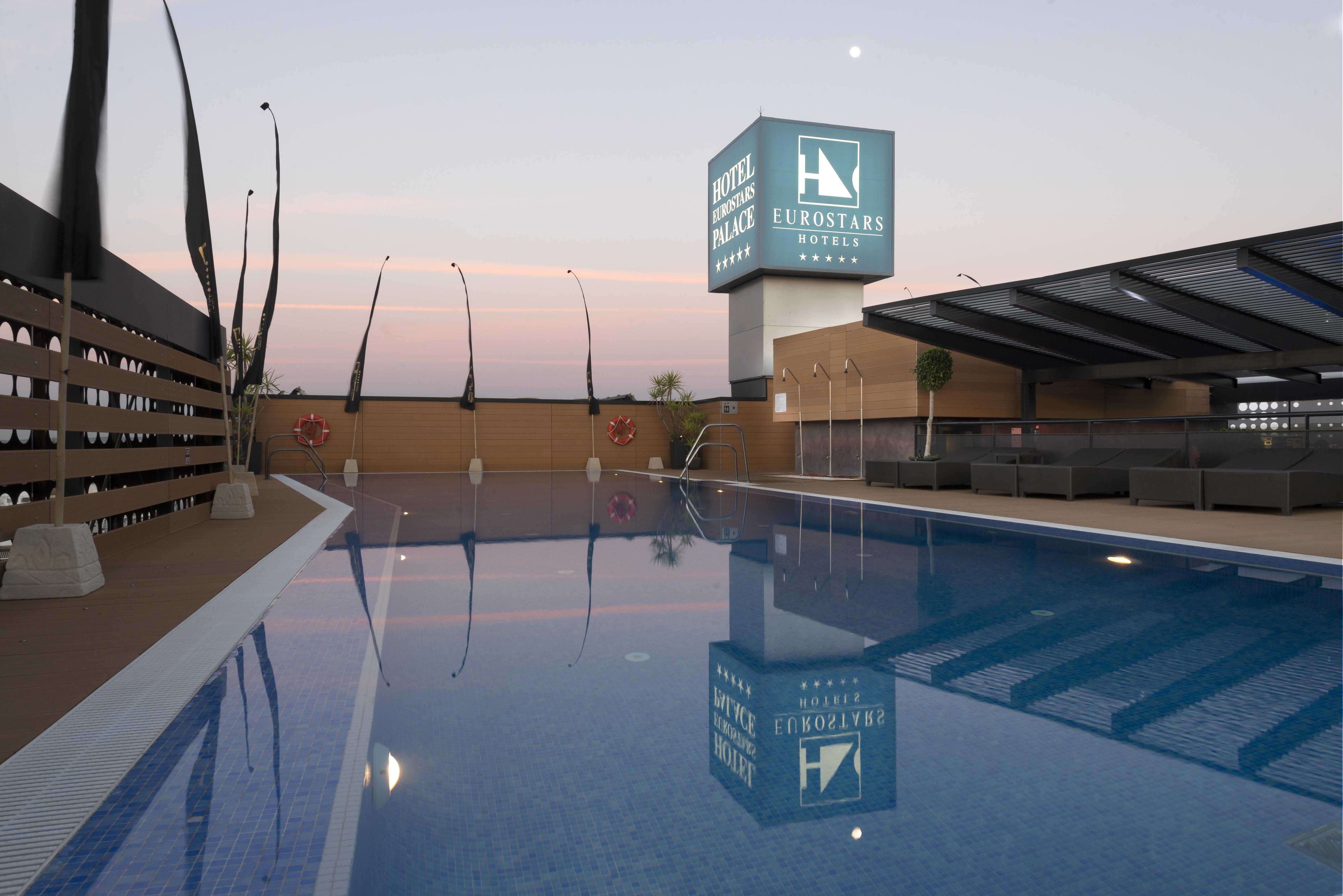 Eurostars Palace Cordoba Luaran gambar The photo shows a rooftop space featuring a swimming pool. The pool has a clear blue water, and the area around it is designed with modern aesthetics, including a wooden deck and comfortable seating. In the background, there is a prominent sign for "
