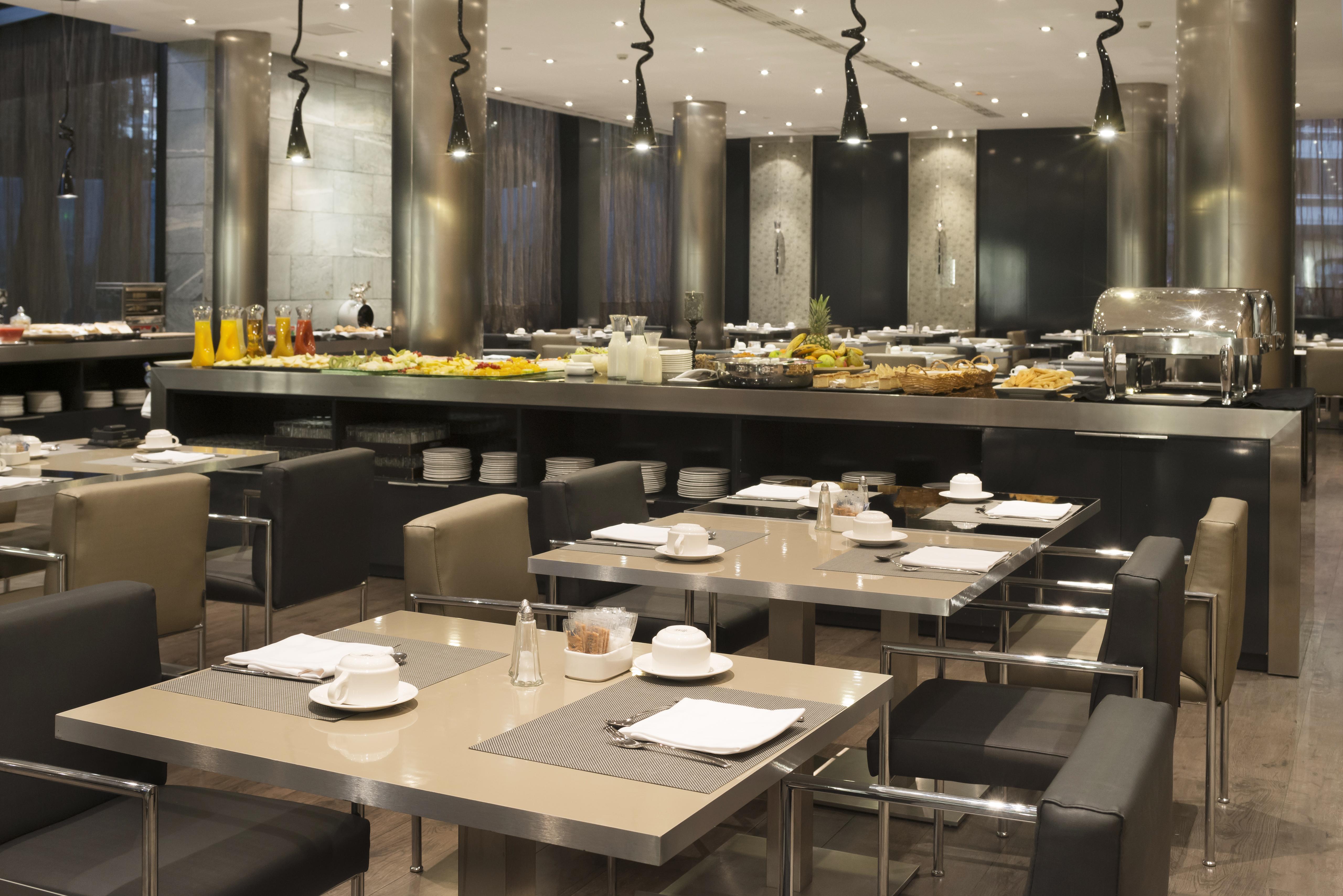 Eurostars Palace Cordoba Luaran gambar The photo depicts a modern restaurant interior featuring a spacious dining area with several tables. Each table is set with plates and cutlery, suggesting it's prepared for guests. In the background, there is a buffet station with an extensive displa