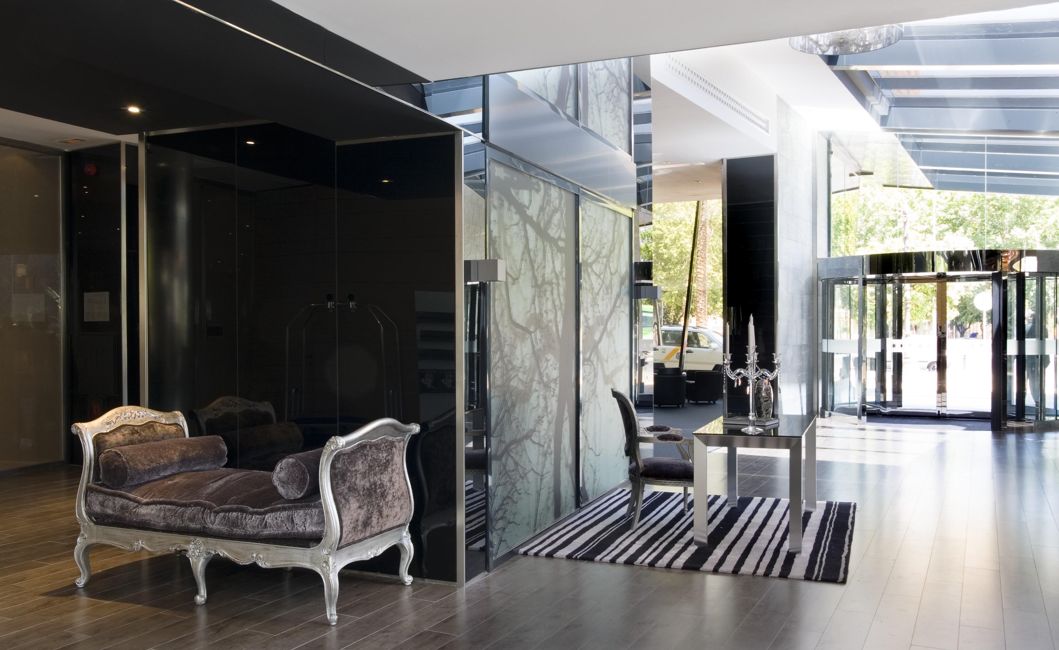 Eurostars Palace Cordoba Luaran gambar The photo features a modern and stylish interior space, likely a lobby or reception area. On the left, there is an elegant couch with ornate detailing, set against dark, reflective walls. The floor is wooden and has a sleek design. To the right, ther