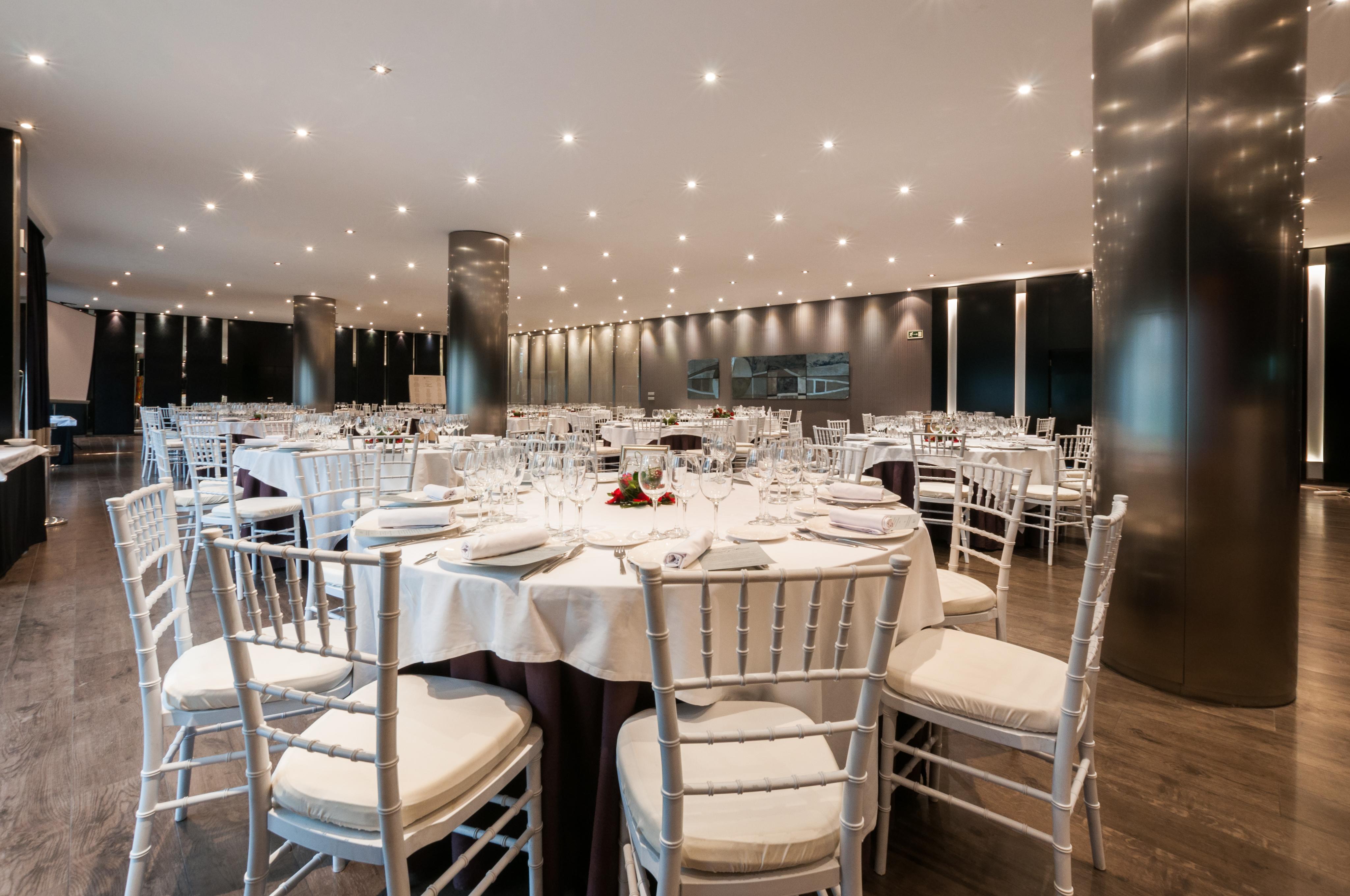 Eurostars Palace Cordoba Luaran gambar The photo shows an elegant dining setting in a spacious restaurant. There are several round tables, each with white tablecloths and neatly arranged place settings, including glasses, plates, and utensils. The chairs are white with padded seats, provi