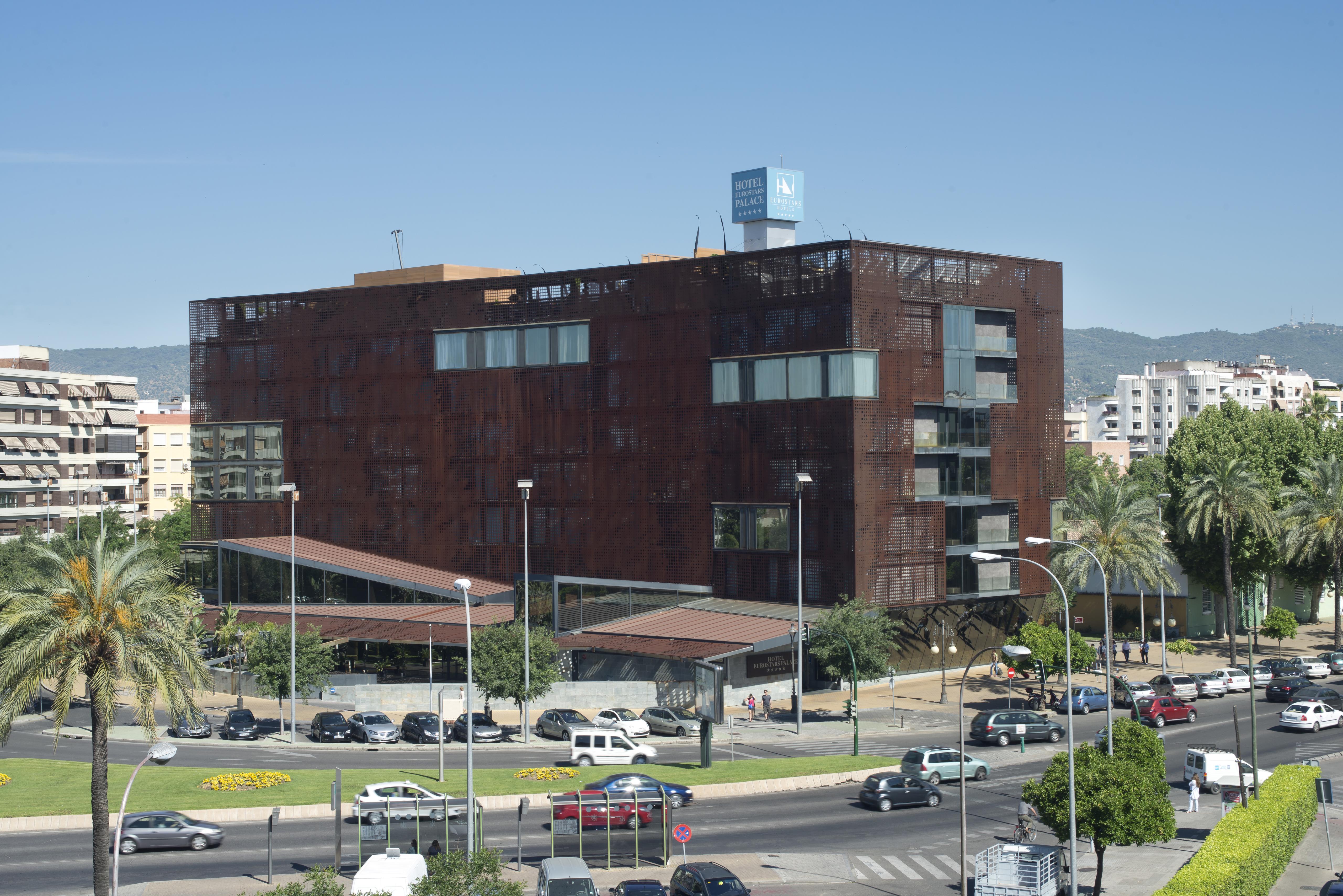Eurostars Palace Cordoba Luaran gambar The photo shows a modern building characterized by a distinctive brown, rust-like exterior, which gives it an industrial appearance. The structure has multiple large windows, allowing for natural light to enter. There are several palm trees surroundi
