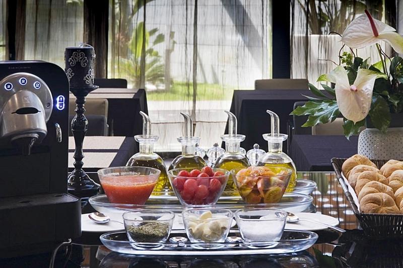 Eurostars Palace Cordoba Luaran gambar The photo displays a stylish breakfast or brunch spread on a table. In the foreground, several small glass containers hold various ingredients: there are glasses filled with different types of oil, a bowl of fresh red tomatoes, a bowl of mixed fruit,