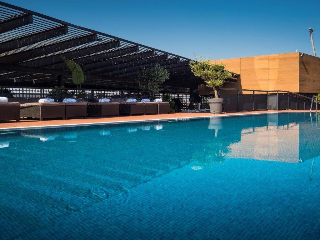 Eurostars Palace Cordoba Luaran gambar The photo shows a rooftop swimming pool with a clear, vibrant blue surface reflecting the sky. Surrounding the pool are comfortable lounge chairs, some shaded by a modern overhead structure. The area is accented with potted plants, adding greenery to