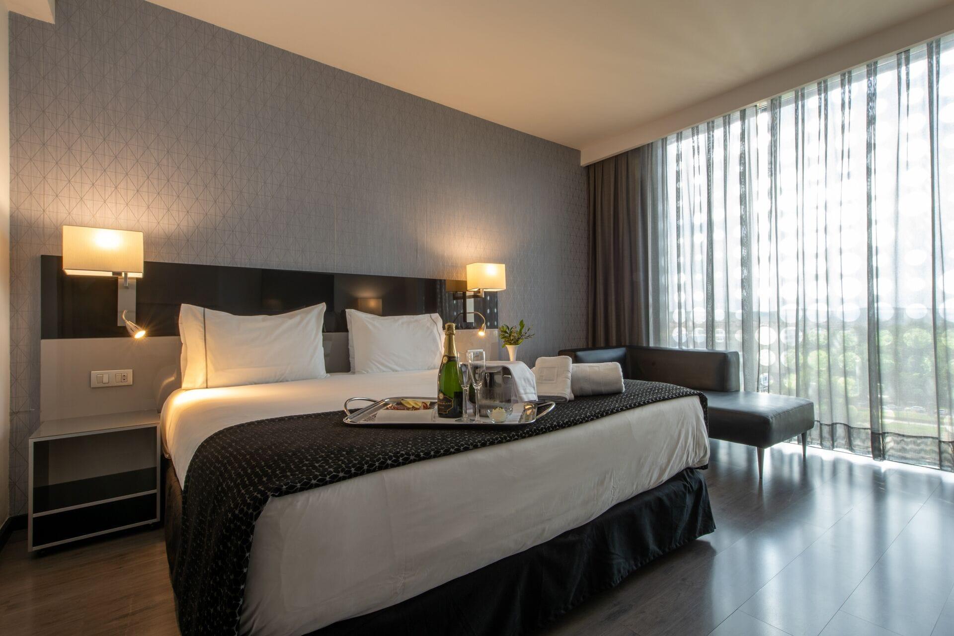 Eurostars Palace Cordoba Luaran gambar The photo shows a modern hotel room featuring a large bed with crisp white linens and dark throw blankets. On either side of the bed, there are bedside lamps providing soft lighting. The room has a sleek design with a neutral color palette, including
