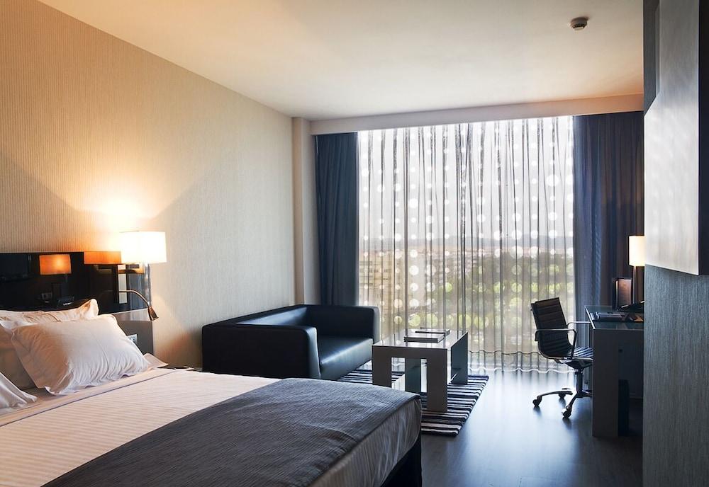 Eurostars Palace Cordoba Luaran gambar The photo shows a modern hotel room featuring a king-sized bed with crisp white linens and a dark gray throw blanket. Beside the bed, there are lamps for lighting. To one side, there is a small seating area with a black leather couch and a coffee tab