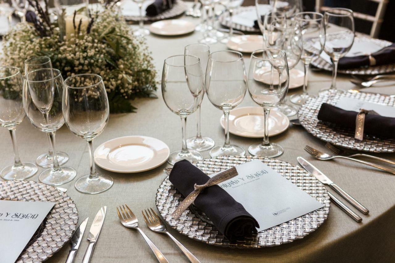 Eurostars Palace Cordoba Luaran gambar The photo shows a beautifully arranged dining table set for an event. The table has a neutral-colored tablecloth and is adorned with elegant place settings. Each setting features a decorative plate with a textured silver charger underneath, and a fol